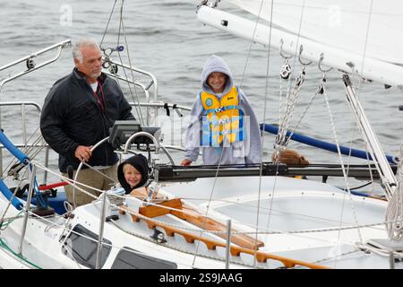 Ein Mann mit Kindern segelt sein Boot während des Tall Ships Festivals in den Hafen von Duluth. Stockfoto