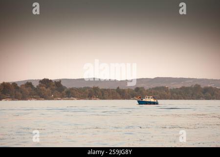 BELGRAD, SERBIEN - 12. OKTOBER 2024: Ein kleines Freizeitboot fährt entlang der Donau in der Nähe von Belgrad, Serbien, im warmen Licht des späten Nachmittags. Die CA Stockfoto