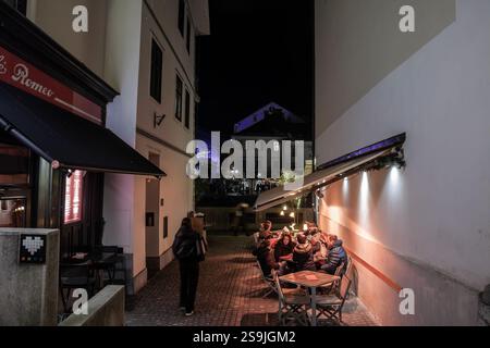 LJUBLJANA, SLOWENIEN - 26. DEZEMBER 2024: Abendliche Szene der Café-Terrasse im Stadtzentrum von Ljubljana im Winter, mit Menschen, die unter warmen Lichtern gesellig sind A Stockfoto