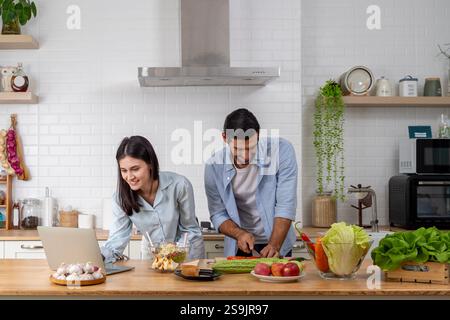 Online-Shopping für Paare mit mehreren Rassen. Ich habe einige Rezensionen über Restaurants gelesen, um sie zu überprüfen. Eine Frau, die einen Laptop benutzt und als Mann lächelt, serviert Frühstück. Stockfoto