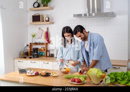 Ein junges verliebtes Paar in der Küche. Glückliches Paar, Das Zu Hause Zusammen Essen Kocht. Lächelndes Paar Packt Gemüse In Der Küche Aus. Stockfoto