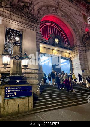 Der Bahnhof Waterloo in London, die Fassade und die Treppe führt nach innen, wo Leute ein- und ausgehen. Rote Leuchten beleuchten die Front mit Personen. Stockfoto