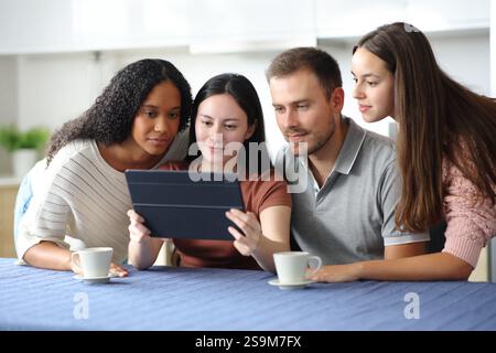 Vier interrassische Freunde überprüfen den Inhalt von Tablets in der Küche zu Hause Stockfoto