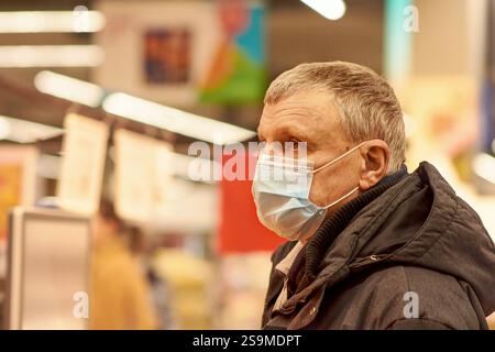 Ein 65-jähriger Mann mit blauer medizinischer Maske holt Lebensmittel in einem Supermarkt ab. Lebensmitteleinkauf während der Coronavirus-Pandemie. Stockfoto