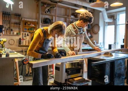 Zimmermannspaar, das Holzbalken auf einer elektrischen Kreissäge schneidet. Anleitung für Anfänger im Basteln Stockfoto