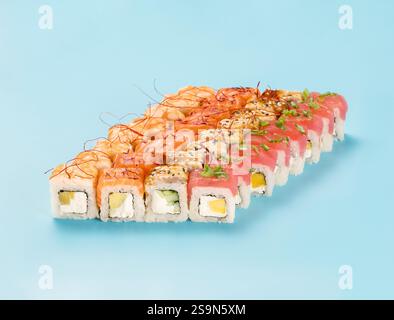 Philadelphia Roll Set mit Mango, Gurke und Avocado, gewickelt mit perfekt gewürztem Sushi-Reis und frischem Lachs, Thunfisch, Garnelen und geräuchertem Aal, dekorierten Chili-Garnen. Isoliert auf hellblauem Hintergrund Stockfoto