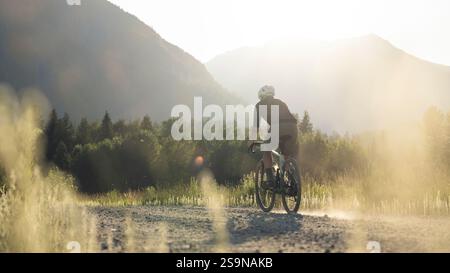Schotterbiker auf einem unbefestigten Weg während der goldenen Stunde in einem ruhigen Tal. Stockfoto