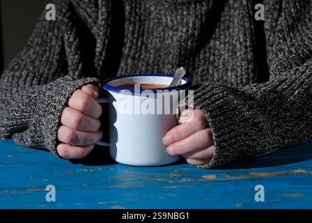 Ältere Frau mit Metallbecher mit heißer Schokolade auf blau lackiertem Tisch Stockfoto