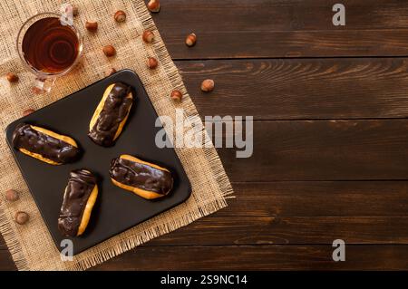 Eclairs mit schwarzer Schokolade und weißer Schokolade mit Pudding in Teller auf Holztisch. Traditionelles französisches Dessert. Eclair Pastery Konzept Stockfoto