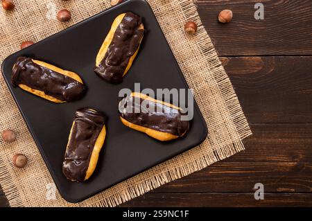 Eclairs mit schwarzer Schokolade und weißer Schokolade mit Pudding in Teller auf Holztisch. Traditionelles französisches Dessert. Eclair Pastery Konzept Stockfoto