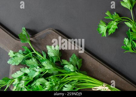 Bund frischer Petersilie mit Schneidebrett auf rustikalem Tisch, grünes Blattgemüse, gesunde Ernährung (Petroselinum crispum) Stockfoto