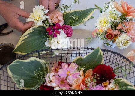 Person, die verschiedene bunte Blumen und Grün in Vasen arrangiert Stockfoto