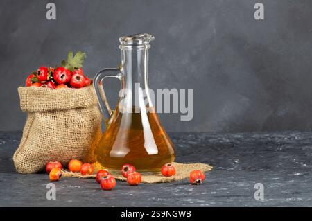 Glasflasche Weißdornessig mit frischen reifen roten/gelben Weißdornfrüchten auf rustikalem Hintergrund. Crataegus monogyna Beeren Stockfoto