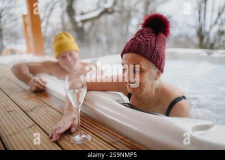 Reizende Senioren, die während des Badens im Whirlpool Champagner trinken. Romantischer Wellness-Kurzurlaub mit Spa am Valentinstag-Wochenende. Stockfoto