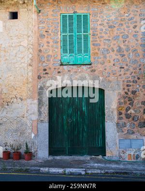 Traditionelles Steinhaus auf Mallorca mit kleinem Fenster, einer alten grünen Tür, Topfblumen auf dem Boden, die im rustikalen mediterranen Stil stehen. Stockfoto