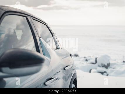 Reisen im Winter - Teil des Autos am Ufer eines riesigen gefrorenen Sees. Linke Seite des silbernen SUV auf Schnee am sonnigen Nachmittag. Stockfoto