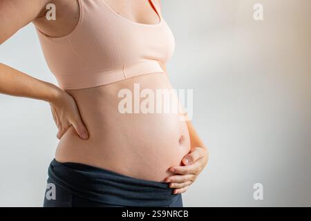 Eine schöne schwangere Frau, die ihren Bauch sanft berührt, während sie sich in einer entspannten und friedlichen Haltung befindet Stockfoto