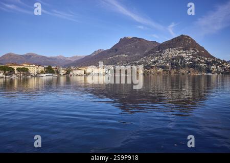 Berge, Dorf, See, Ufer, allgemeine Entwicklung, Reflexionen auf der Wasseroberfläche, blauer Himmel, Schleierwolken, Luganer See, Lugano, Bezirk Lugano, c Stockfoto