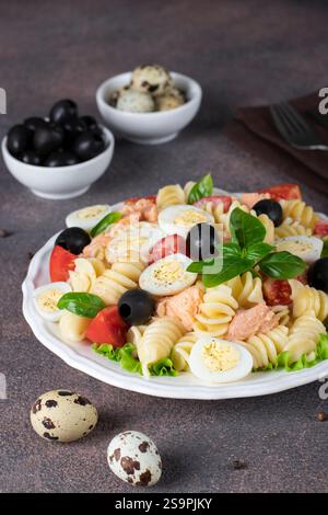 Salat aus der Dose mit Nudeln, Kirschtomaten, Wachteleiern, Basilikum und schwarzen Oliven Stockfoto