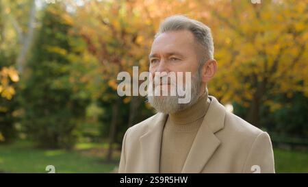 Eleganter reifer grauhaariger Mann, der allein auf der Straße im Herbst spaziert, in der Parkanlage ruhig nachdenklich, kaukasischer Senior 60er Jahre Geschäftsmann, spazieren in der Natur im Freien, alt Stockfoto