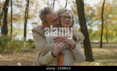 Kaukasisches Ehepaar umarmen sich zusammen im Herbstpark Seniorenmann umarmt hinter reifer Frau lieblich umarmt Familienliebe Moment zwei glücklich Stockfoto