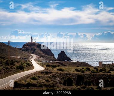 Ein malerischer Blick auf die Küste mit einem Leuchtturm auf einer felsigen Klippe mit Blick auf das Meer. Der Himmel ist teilweise bewölkt und das Sonnenlicht reflektiert auf dem Wasser. Stockfoto