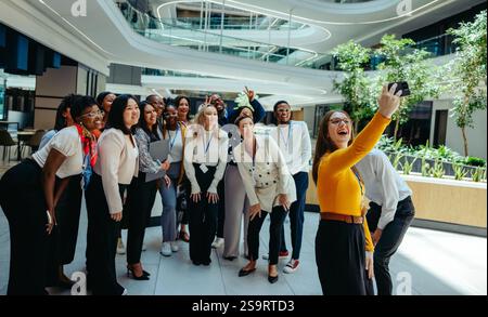 Eine fröhliche und vielfältige Gruppe von Kollegen, die ein Selfie in einer modernen Büroumgebung machen. Die Umgebung ist hell und geräumig, mit Teammitgliedern Stockfoto