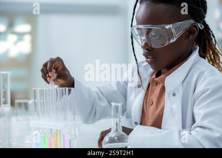 Lächelnde Forscherin mit Petrischale und Kolben zur Analyse chemischer Flüssigkeiten im Labor Stockfoto