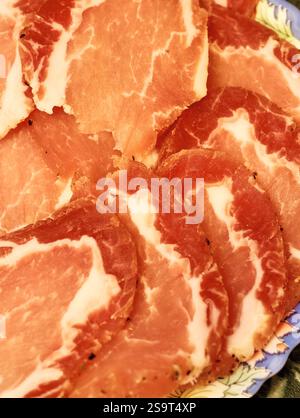 Köstlich geschnittenes geräuchertes Fleisch, kunstvoll auf einem dekorativen Teller mit satten Farben und Texturen in einem kulinarischen Ambiente angeordnet Stockfoto