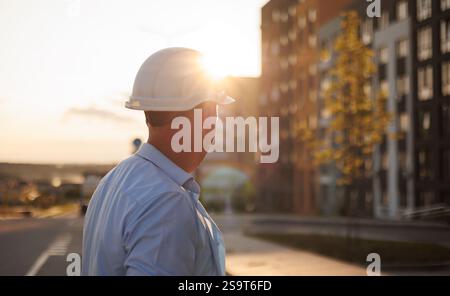 Rückansicht eines männlichen Architekten, Bauherr in Schutzhelm Inspektionen, untersucht die Sicherheit des fertigen neuen Projekts eines modernen Wohngebäudes. Konstruktion Stockfoto
