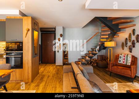 Ein Weitwinkelblick auf ein luxuriöses Wohnzimmer und eine hängende Treppe, die die einzigartige Ästhetik der Holzeinrichtung des Apartments zeigt. Immobilien in Stockfoto