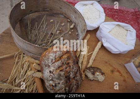 Handgemachtes und hausgemachtes Sauerteigbrot mit Oliven auf Holztisch, dekoriert mit einer Nudelnadel und Werkzeugen zum Sieben von Brotkrumen mit Sesam Stockfoto