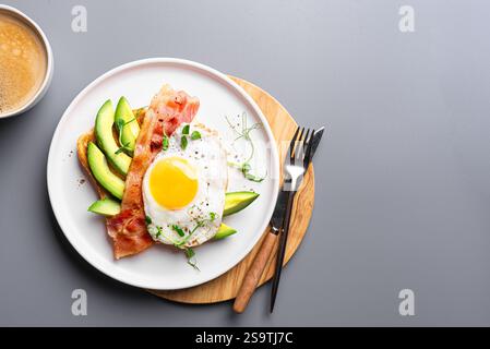 Frühstückssandwich mit Spiegelei, Speck, Avocado und Mikrogrün auf grauem Hintergrund, Kopierraum. Bio-Ei mit Speck auf Toast und morgens Cappucci Stockfoto