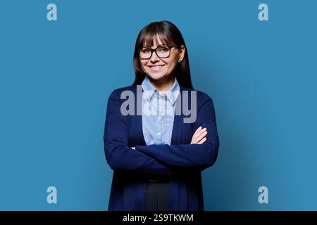 Porträt reife Geschäftsfrau mit gekreuzten Armen auf blauem Hintergrund Stockfoto