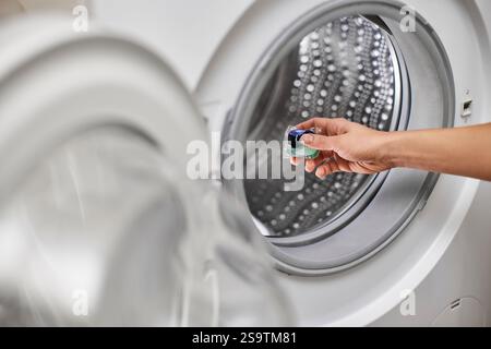 Weibliche Hand, die Waschmittelkapsel in die Waschmaschine gibt Stockfoto