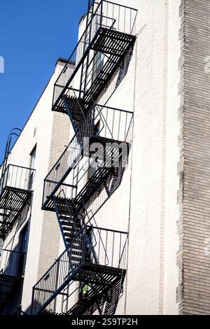 Spiralförmige Feuertreppen sind an ein Backsteingebäude angeschlossen. Die schwarze Metallstruktur hebt sich vom klaren blauen Himmel ab Stockfoto