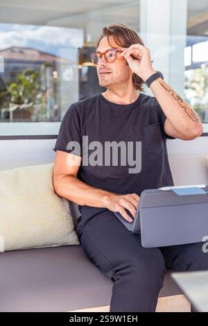 Ein Hipster-Mann in einem schwarzen Hemd berührt seine Brille, während er mit diesem Tablet arbeitet. Produktivitäts- und Konzentrationsbegriff Stockfoto