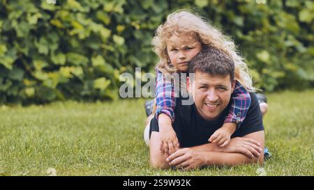 Vater und Tochter genießen einen verspielten Moment zusammen, liegen auf dem Gras in einem sonnigen Garten und genießen die Zeit der Familie Stockfoto