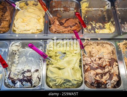 In Edelstahlbehältern werden verschiedene köstliche Eisaromen präsentiert. Schaufeln und Behälter sind für Kunden bereit. Die cremige Textur Stockfoto