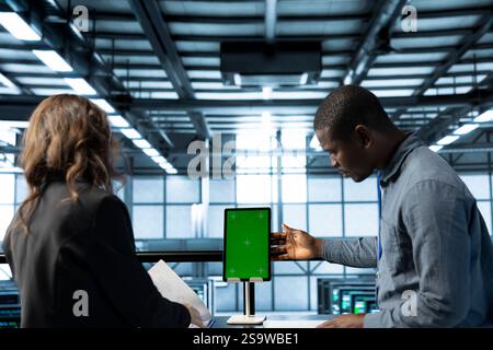 Techniker im Rechenzentrum, die ein Mockup-Tablet mit grünem Bildschirm verwenden, Hardwarediagnosen überprüfen, fehlerzustände löschen, Gerätekonfigurationen anpassen und Firmware-Aktualisierungen anwenden Stockfoto