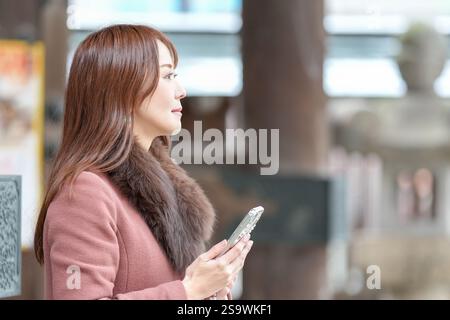 Ein Tor zu einem Schrein in Hakata, Fukuoka, Japan. Langhaarige Frauen in ihren 30ern bedienen Smartphones. Stockfoto