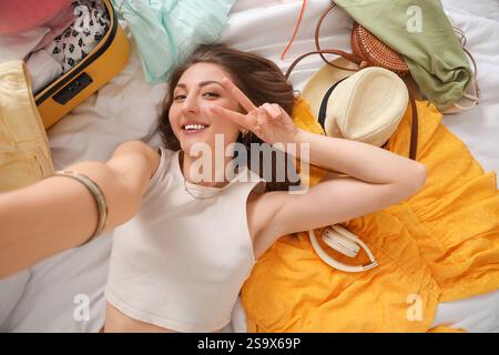 Junge Frau mit Strandaccessoires und Koffer, die Selfie auf dem Bett macht Stockfoto