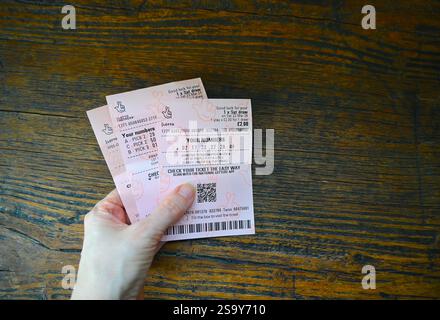 Nationale Lotteriescheine in menschlicher Hand auf dunklem Holz. Stockfoto