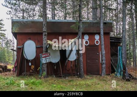 Alte rustikale Scheune im Wald mit lustigen Toilettensitzen, die über der Tür hängen, mit verschiedenen Gegenständen, an einem kühlen Herbstmorgen im November. Stockfoto
