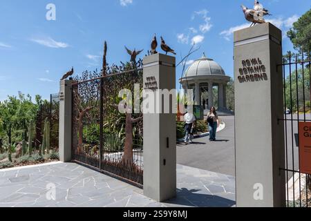 Indische Paare spazieren zu kunstvollen Eisentoren mit Elsterskulpturen auf den Torpfosten am Eingang zu den Royal Botanic Gardens, Melbourne, Australien Stockfoto