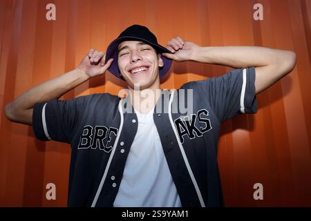 Lächelnder junger Mann, der seinen Hut hält und lacht Stockfoto