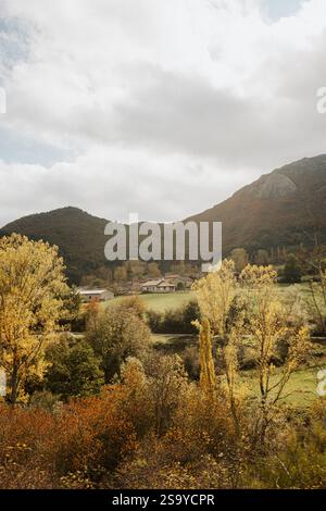 Malerische Herbstlandschaft in Asturien, Spanien, mit bunten Bäumen, sanften grünen Hügeln und einem kleinen ländlichen Dorf inmitten der Berge Stockfoto