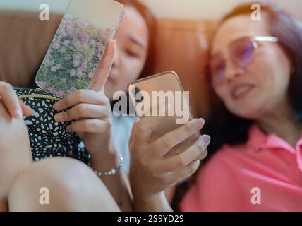 Zwei junge Erwachsene Freunde lachen zusammen und nutzen ihre Smartphones zu Hause online. Selektiver Fokus auf die Hände. Stockfoto