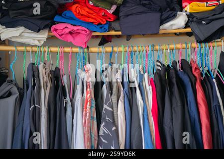 Viele Klamotten auf Kleiderbügel. Verschiedene legere Männerkleidung in verschiedenen Farben auf Kleiderbügeln im männlichen Schlafzimmer. Stockfoto