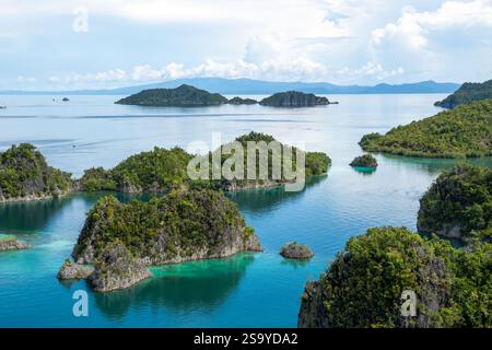Aus der Vogelperspektive auf die üppig grünen Pianemo-Inseln in türkisfarbenem Wasser, mit Booten und fernen Inseln unter klarem Himmel, Fam-Inseln, Waigeo, Raja Ampat, West Stockfoto